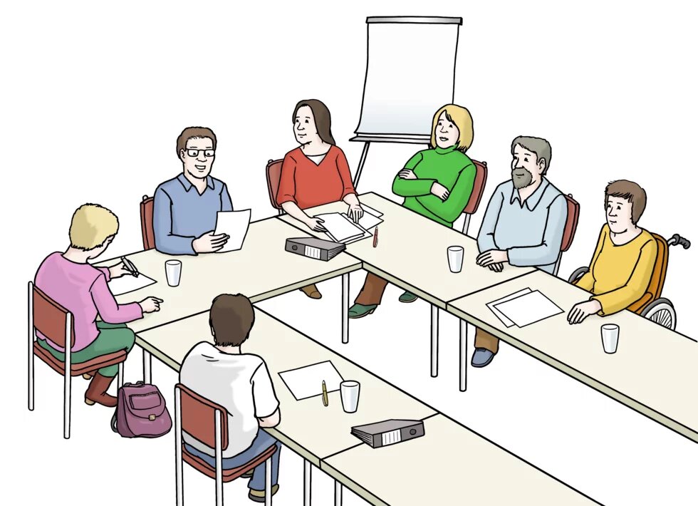 Menschen sitzen an Tischen, die in einer U-Form aufgestellt sind. Im Hintergrund steht ein Flipchart.